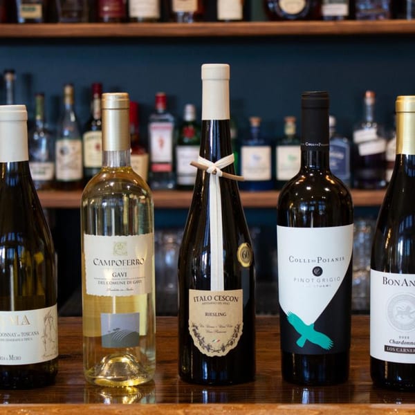 Five bottles of Italian wine, including white and red varieties, displayed on a wooden bar.
