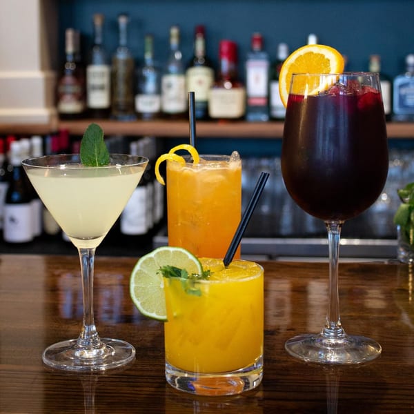 Four colorful cocktails, including sangria, on a wooden bar with liquor bottles in the background.