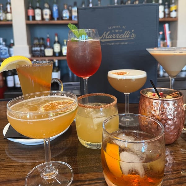 A variety of colorful cocktails and drinks on a wooden bar, with a Marrelli's menu in the background.