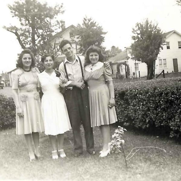 Four young people, three women and one man, posing outdoors in 1940s attire.