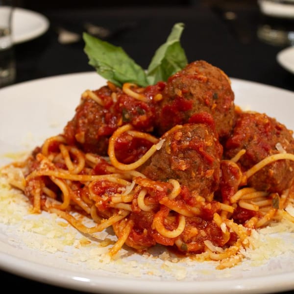 Spaghetti and meatballs with tomato sauce, Parmesan cheese, and basil on a white plate.