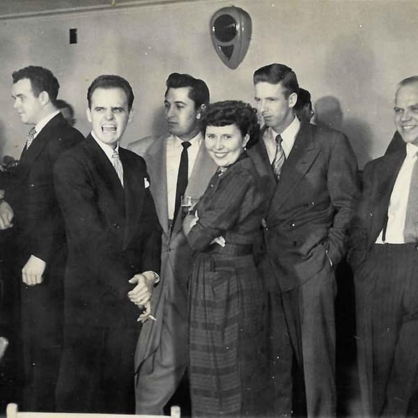 Black and white photo of a group of people, some smiling, in a vintage setting.