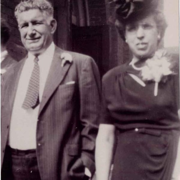 Black and white photo of a smiling man in a suit and a woman in a dress with a corsage.