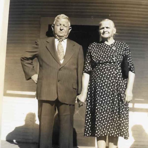 Sepia-toned portrait of an older man in a suit and a woman in a polka-dot dress holding hands.