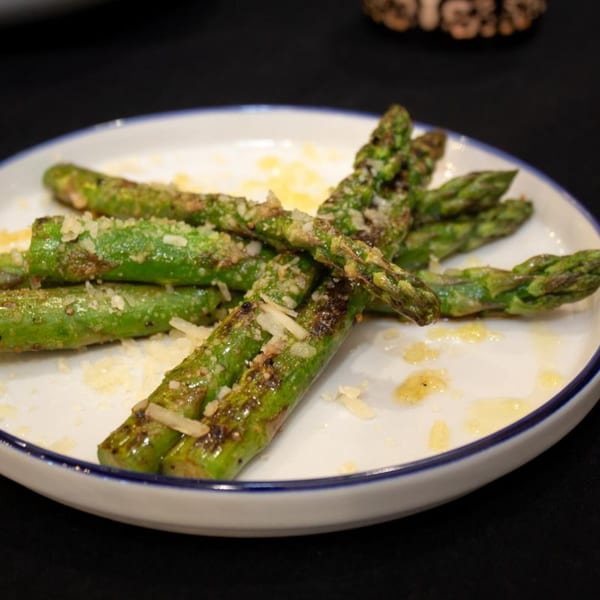 Grilled asparagus spears topped with grated Parmesan cheese and olive oil on a white plate.