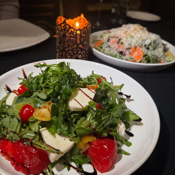 Two Italian salads, one with mozzarella and tomatoes, on a dark table with a lit candle.